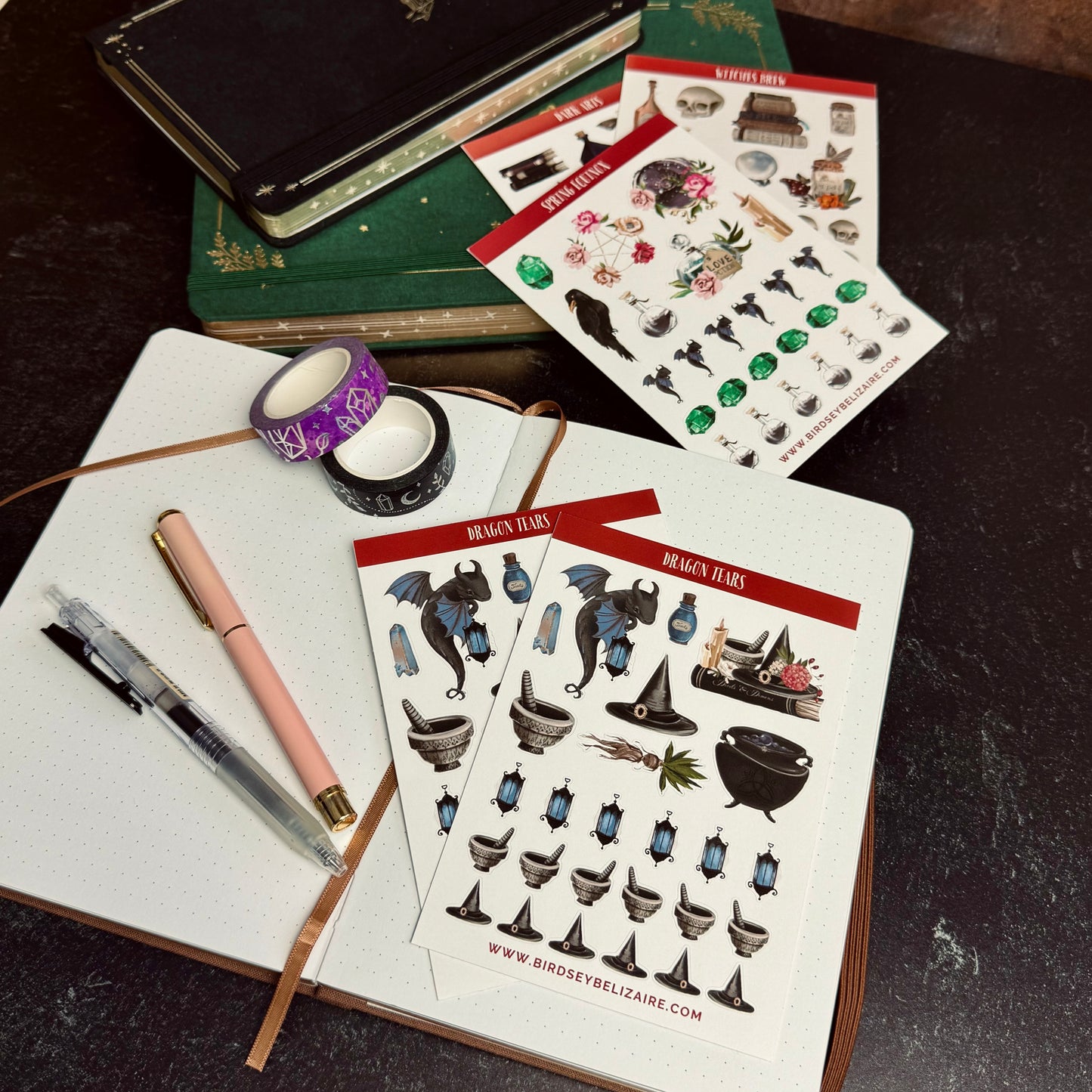 Sticker sheets with fantasy-themed designs on a notebook with pens and tape.
