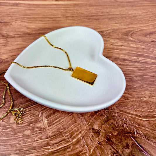 Gold necklace laying on a heart-shaped trinket tray made from white jesmonite sat on a wooden surface