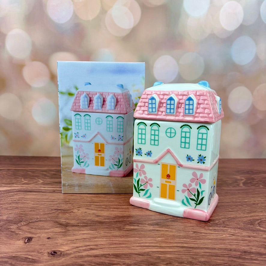 White house-shaped oil burner and wax warmer, featuring pink tiled roof, a yellow door, floral motifs in a 3 storey regency style. Burner and matching box sits on a wooden surface against a blurred background.