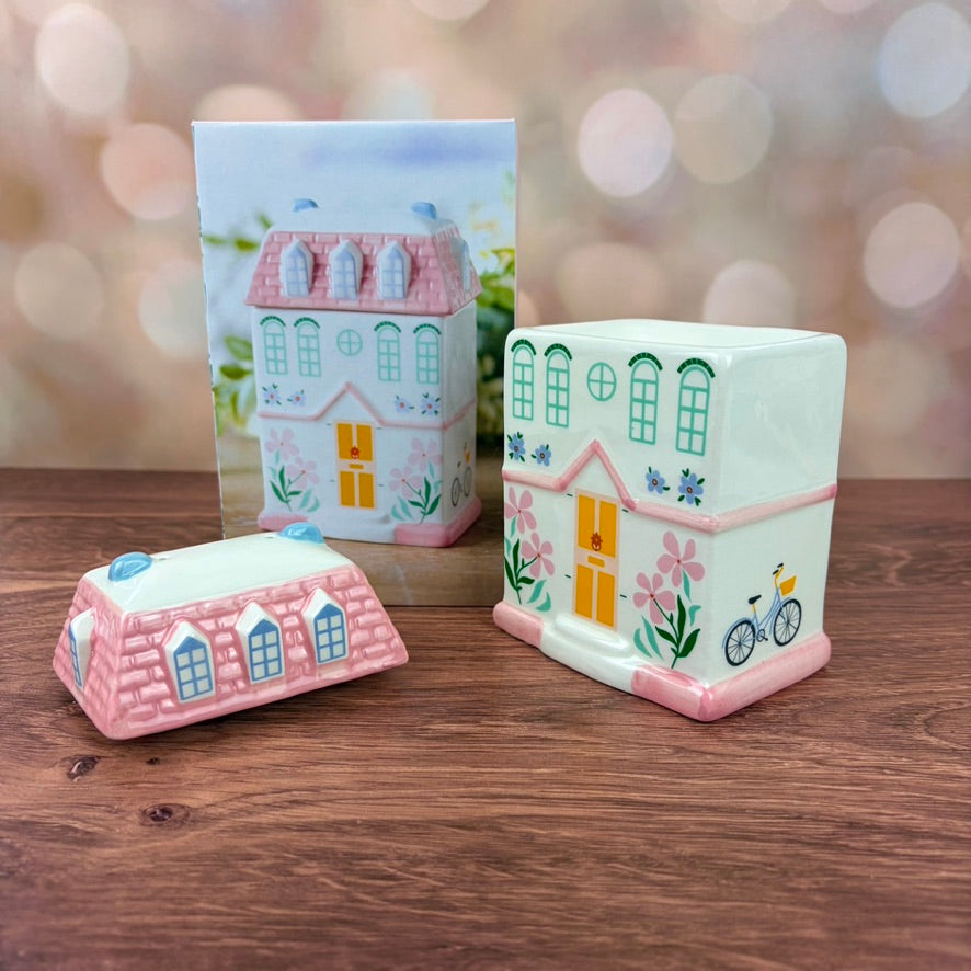 White house-shaped oil burner and wax warmer, featuring pink tiled roof, a yellow door, floral motifs in a 3 storey regency style. Burner and matching box sits on a wooden surface against a blurred background.