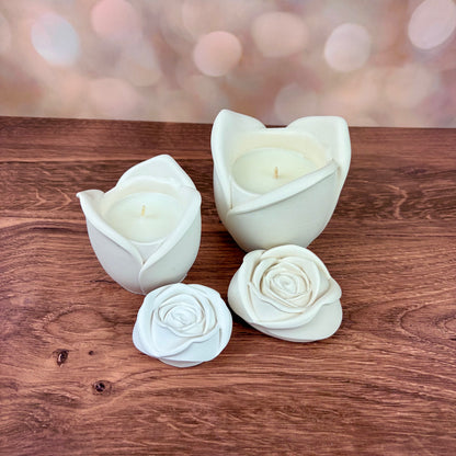 White rose-shaped candles, in two sizes with sculpted petal rose lids placed in front of each candle, all sat on a wooden surface with a blurred pink bokeh background