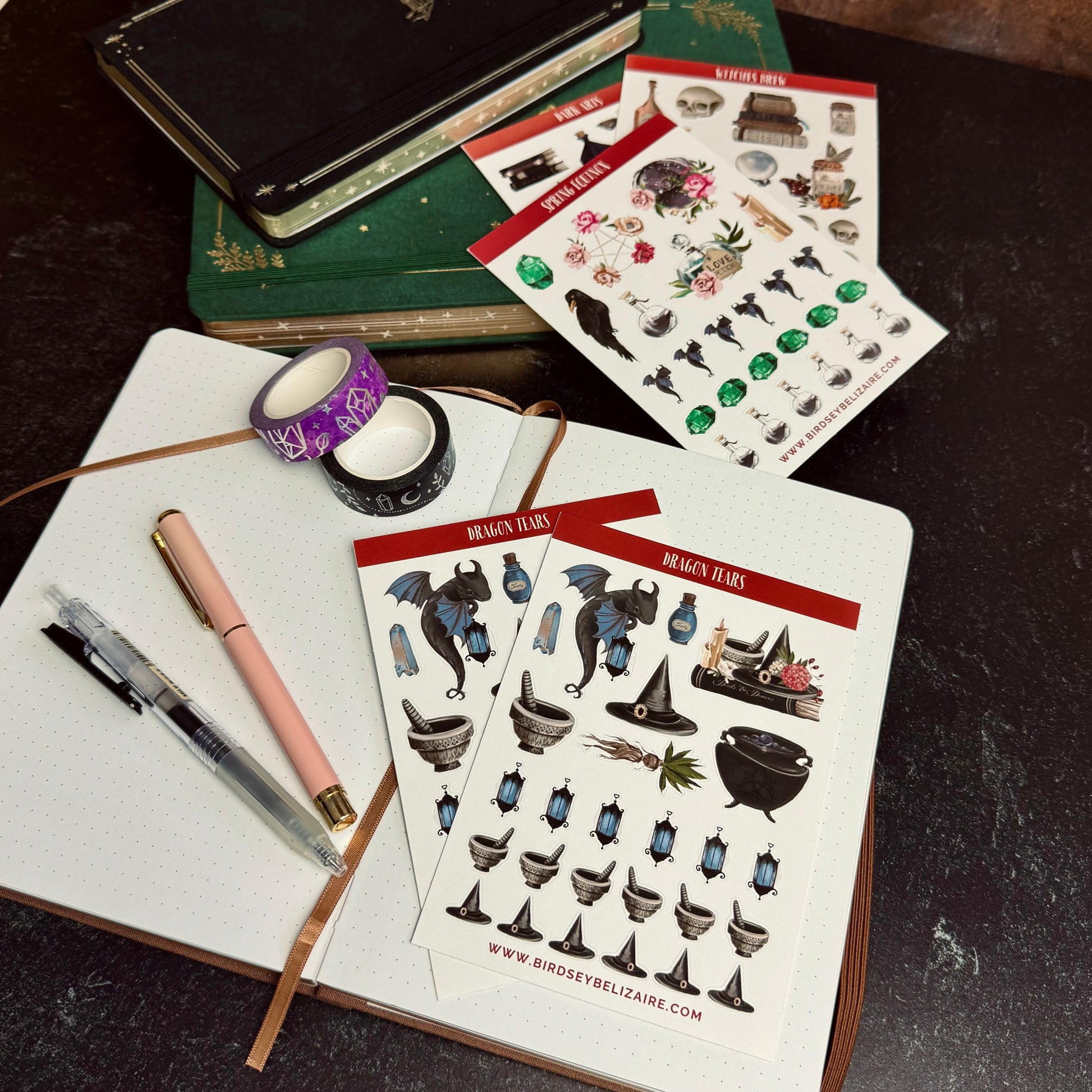 Sticker sheets with fantasy-themed designs on a notebook with pens and tape.