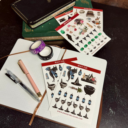 Sticker sheets with fantasy-themed designs on a notebook with pens and tape.